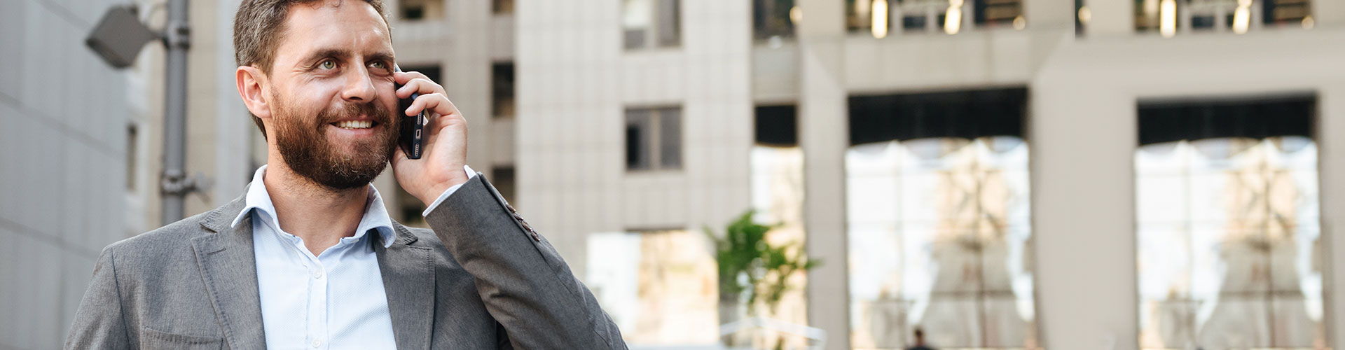 Seguros Banca Privada - Hombre de negocios con un traje gris y camisa blanca hablando por el móvil junto a un edificio en una ciudad Seguros Banca Privada - Hombre de negocios con un traje gris y camisa blanca hablando por el móvil junto a un edificio en una ciudad